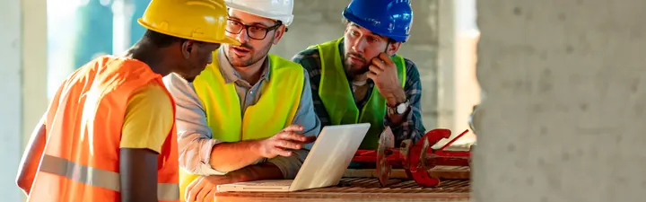 Bauleiter und Poliere besprechen Pläne am Laptop auf der Baustelle